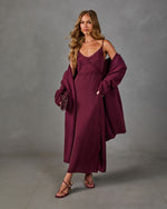 Woman wearing a burgundy satin lace-trim midi slip dress with slit, oversized knit cardigan, mini bag and strappy heeled sandals