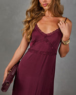Burgundy satin maxi slip dress with lace trim and spaghetti straps, styled with gold bangles and a woven burgundy clutch