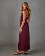 Woman in a burgundy satin maxi dress with lace trim and thin straps, styled with gold bracelets and strappy heeled sandals