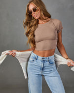 Woman wearing ribbed taupe crop top, light wash high-waist jeans, round sunglasses, holding white cardigan, fashion editorial style