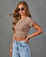Woman wearing taupe ribbed crop top with short sleeves and high-waist light wash jeans, styled with gold hoop earrings and sunglasses