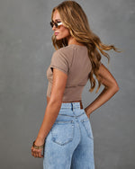 Woman wearing ribbed mocha crop top and high-waist light wash flare jeans, posed from behind, with sunglasses and gold bangles