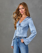 Woman wearing light blue satin corset top with bell sleeves and tie neckline, paired with high-waist blue jeans