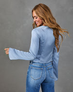 Woman modeling light blue satin bell-sleeve top with high-low hem, paired with medium-wash skinny jeans, back view.