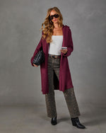 Woman wearing a burgundy hooded long cardigan with leopard print jeans, white tank top, black ankle boots and quilted clutch