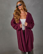 Woman wearing a burgundy oversized hooded knit cardigan with pockets over a white top, leopard print pants and aviator sunglasses
