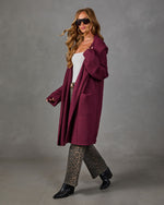 Woman wearing a burgundy oversized hooded cardigan with leopard print jeans, white top, sunglasses and black ankle boots