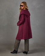 Woman in a burgundy hooded longline cardigan with leopard print jeans and black heeled ankle boots, smiling over her shoulder