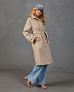 Woman wearing belted beige trench coat, wide-leg jeans, nude heeled sandals, and gray Hamptons baseball cap