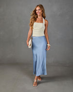 Woman wearing cream ruched halter top and blue satin midi slip skirt with nude sandals and white clutch bag
