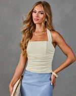 Woman wearing cream ruched halter top and blue satin midi skirt, styled with gold jewelry and white clutch bag