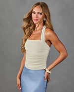 Woman in cream ruched halter top and blue satin midi skirt with layered gold necklaces and pearl earrings