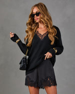 Woman in black lace-trim V-neck sweater, satin lace shorts, cat-eye sunglasses, gold cuff bracelets and black quilted chain bag