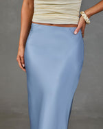 Light blue satin midi skirt paired with cream ruched crop top and gold-studded white bracelet on woman