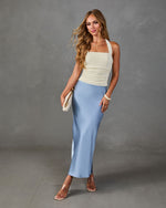 Woman wearing cream ruched halter top and dusty blue satin midi skirt with clear heels and white clutch bag