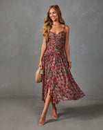 Woman wearing sage green and red floral ruched midi dress with flutter skirt, nude heels, and woven clutch