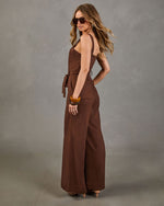 Brown wide-leg linen jumpsuit with tie waist, spaghetti straps, worn with wood bangles and aviator sunglasses