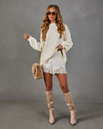 Woman in cream oversized knit sweater, lace-trim satin shorts, tan suede knee-high boots and faux fur chain crossbody bag