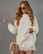 Woman in cream oversized knit sweater, lace-trim satin mini skirt, aviator sunglasses and tan faux fur chain-strap bag