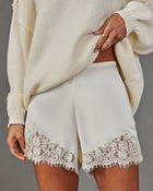 Cream satin shorts with scalloped floral lace hem, styled with an oversized ivory knit sweater and gold stacking rings