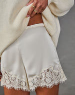 Ivory satin shorts with scalloped floral lace hem, styled with a cream oversized knit sweater and gold stacked rings