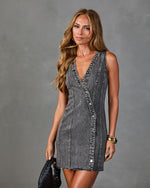 Woman wearing gray acid wash denim mini dress with snap buttons and deep V-neckline, holding black woven bag