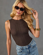 Woman wearing dark brown ribbed knit sleeveless top with high neck, light wash jeans, tortoiseshell sunglasses, gold hoop earrings, and stacked gold bangles