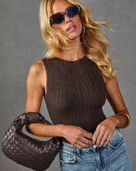 Blonde woman wearing dark brown ribbed knit tank top, woven leather hobo bag, blue jeans, and oval tortoiseshell sunglasses