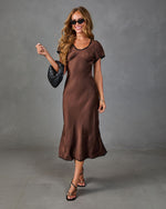 Woman wearing chocolate brown satin midi dress with black trim, short sleeves, paired with strappy heels and woven bag