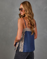 Woman wearing a navy satin cami top with beige lace trim and side slits, viewed from behind with gray jeans and sunglasses