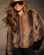 Woman smiling in a faux fur fawn-print bomber jacket with front zipper, aviator sunglasses, gold hoop earrings and black pants
