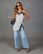 White satin lace-trim cami top styled with light wash wide-leg jeans, black strappy heels, and woven bag on female model