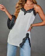 White satin cami top with black lace trim neckline and hem detail, styled with light blue jeans and black woven clutch