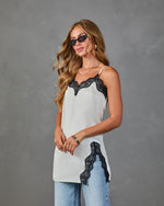 White satin lace-trim cami top with black lace neckline and hem detail, styled with light wash jeans and sunglasses