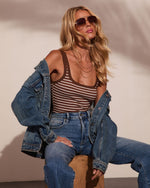 Woman in brown striped tank top, denim jacket, and high-waist jeans wearing aviator sunglasses, casual chic style