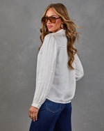 Woman in ivory satin blouse with puff sleeves, dark wide-leg jeans, and tinted aviator sunglasses, looking over her shoulder