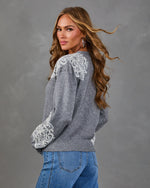Woman in gray knit sweater with white lace shoulder and sleeve appliqué, styled with high-waisted blue jeans and hoop earrings