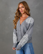 Gray button-front cardigan with white floral lace appliqué on shoulder and sleeves, styled with light wash flare jeans