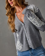 Gray V-neck cardigan with white lace appliqué on sleeves and hem, pearlescent buttons, styled with light-wash blue jeans