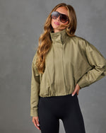 Woman wearing olive green cropped bomber jacket with mock neck and black leggings, styled with oversized aviator sunglasses