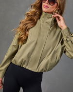 Women's olive green zip-up bomber jacket with mock neck, balloon sleeves, and elastic hem, styled with black leggings