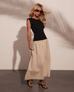 Woman wearing black sleeveless top and beige maxi skirt with black sandals and sunglasses, studio fashion photo