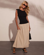 Woman in black sleeveless top and beige midi skirt with black heeled sandals, handbag, and sunglasses, fashion editorial style