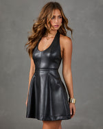 A woman modeling a sleeveless black faux-leather mini dress with a scoop neckline and flared skirt against a textured gray studio background.