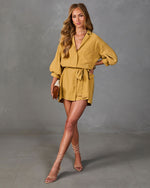 Woman wearing mustard yellow button-up crop top and belted mini skirt set with lace-up nude heels and brown clutch bag