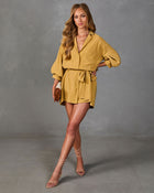 Woman wearing mustard yellow button-up crop top and belted mini skirt set with lace-up nude heels and brown clutch bag