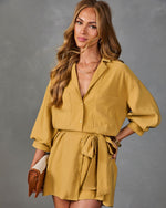 Woman wearing mustard yellow button-down shirt dress with balloon sleeves and tie waist, holding brown leather clutch