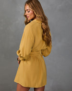 Woman modeling mustard yellow belted shirt dress with long balloon sleeves, viewed from back, against gray background