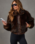 Woman in a brown faux fur bomber jacket with leather trim, black leggings, aviator sunglasses and gold cuff bracelet holding a phone
