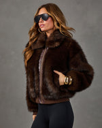 Woman in a brown faux fur bomber jacket with leather zip trim, aviator sunglasses, gold cuff bracelets and black leggings